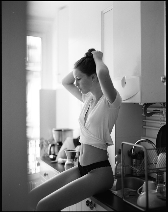 A woman sits on a kitchen counter, tying her hair up in a bun.