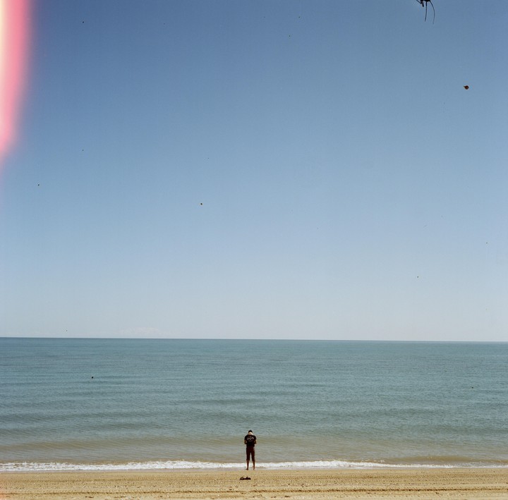 A man stands at the edge of the water on a sandy beach looking out at the sea.