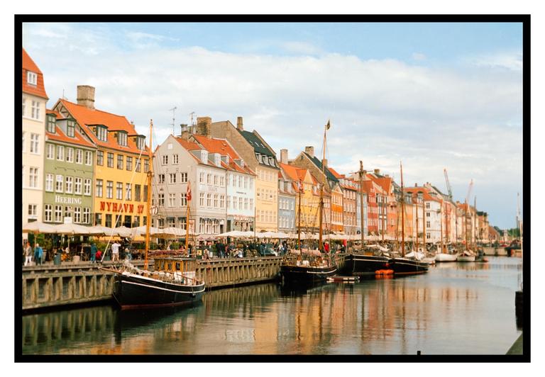 A canal is lined with colorful buildings and boats, with people walking along the waterfront.