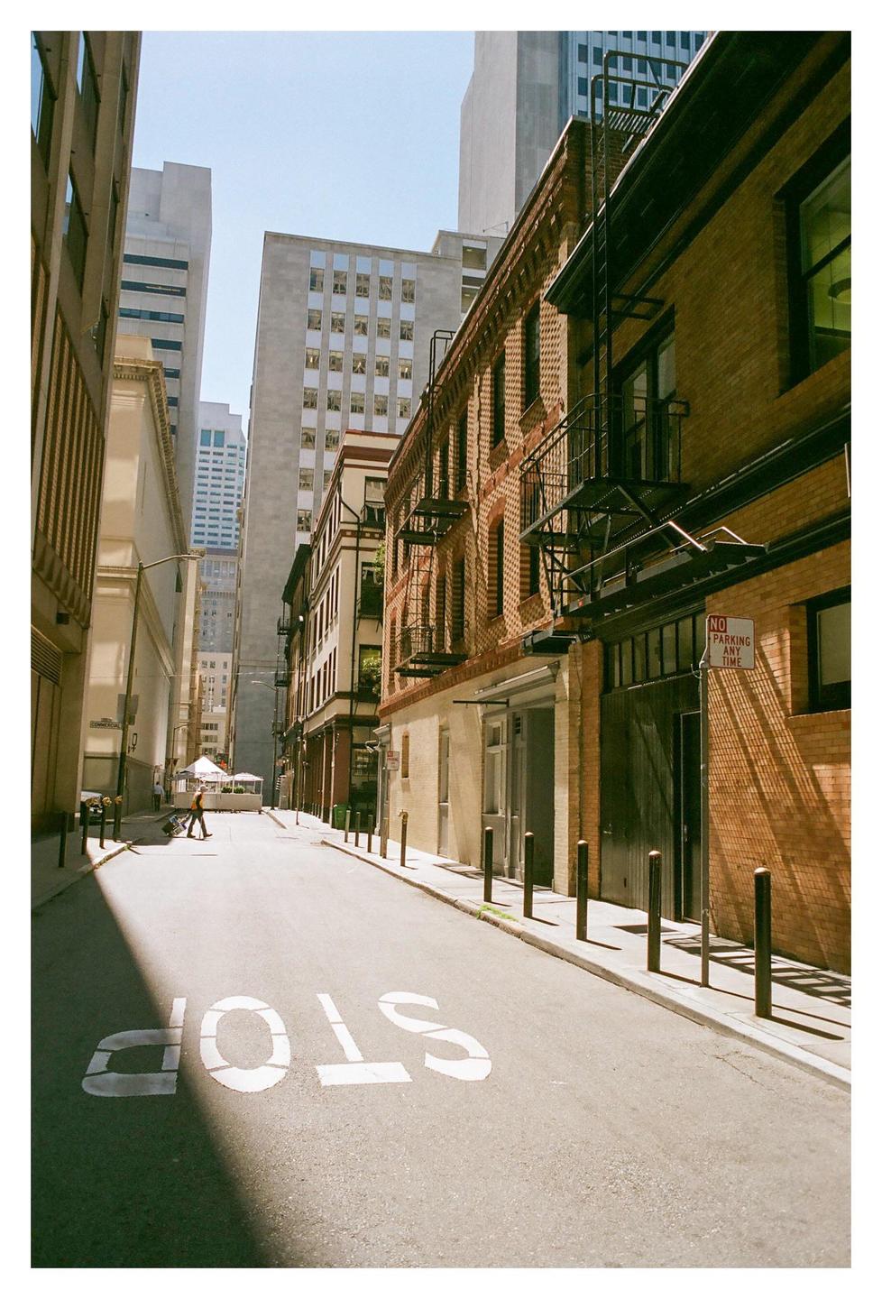 A person walks down a narrow city street with a "STOP" sign painted on the asphalt.