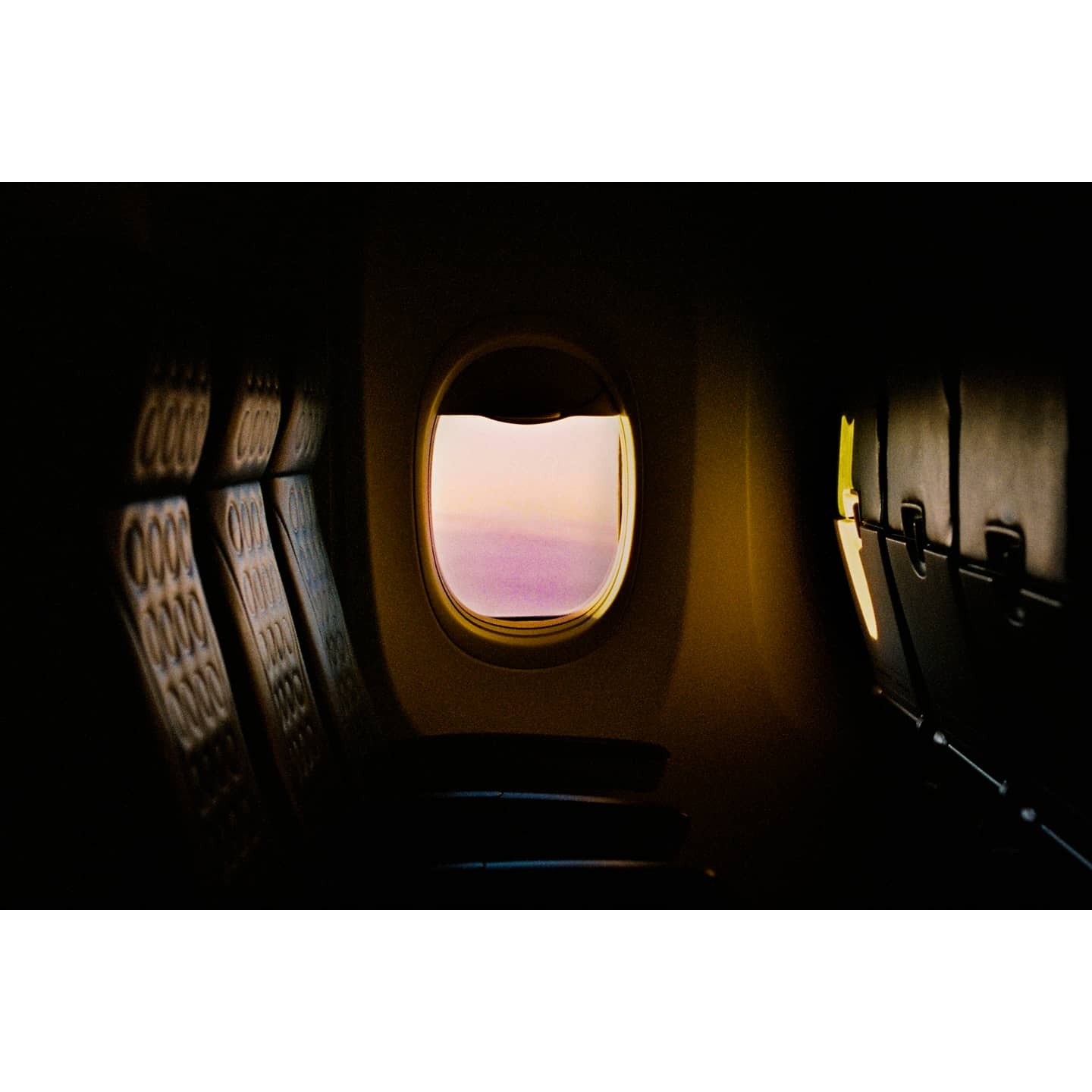 The interior of an airplane cabin is visible with a window looking out onto a pink sky.