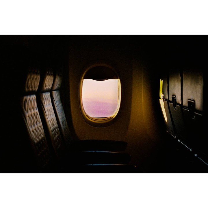 The interior of an airplane cabin is visible with a window looking out onto a pink sky.