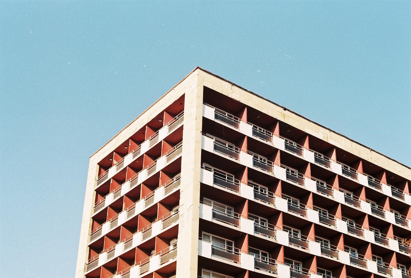 A large building with many balconies is shown from a low angle against a clear blue sky.