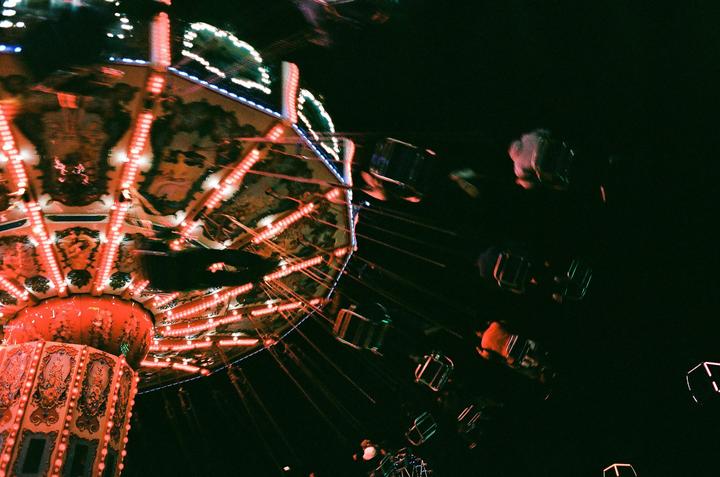 A brightly lit swing ride spins at night, with blurred figures visible in the seats.