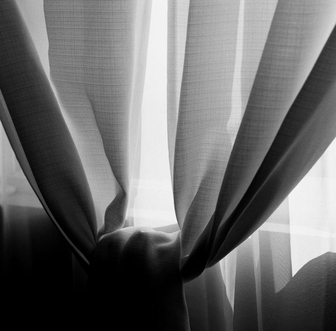 Light shines through sheer curtains that are tied in the middle.