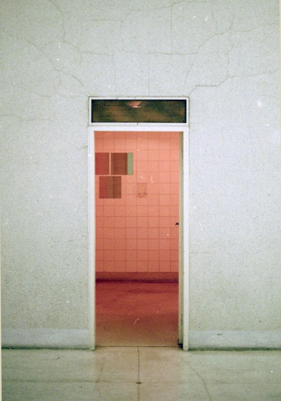 A doorway with a transom window leads into a room with pink tiled walls and a red floor.