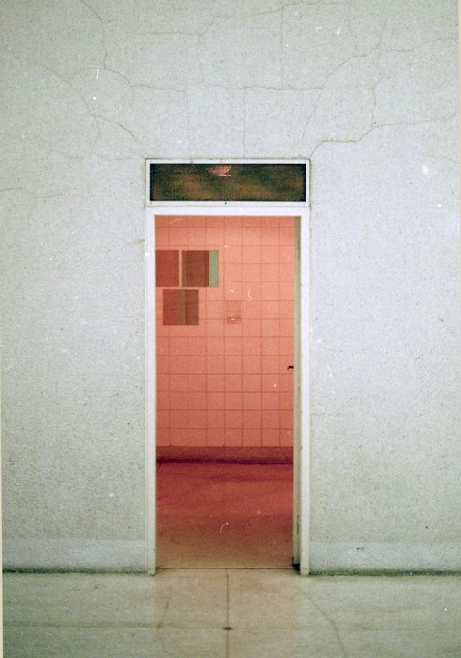A doorway with a transom window leads into a room with pink tiled walls and a red floor.