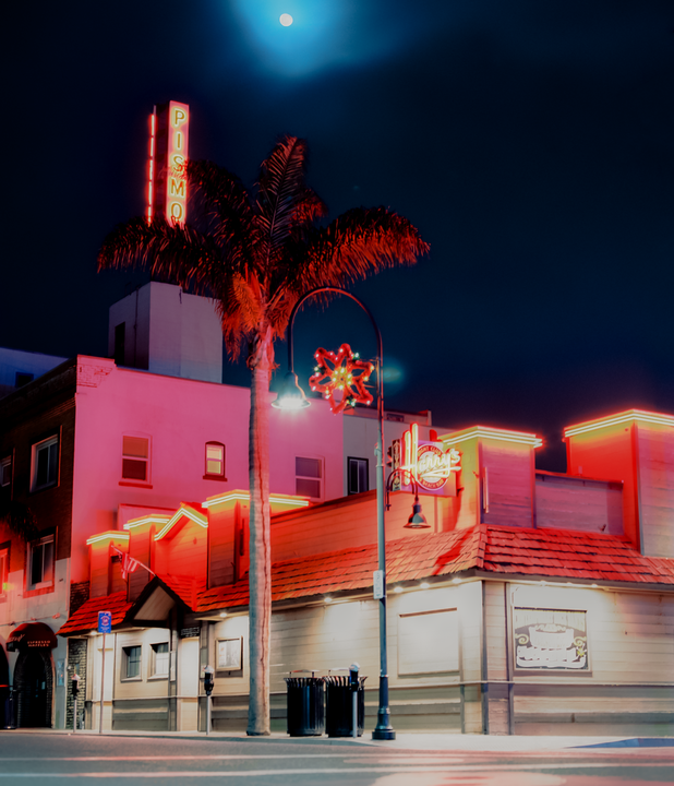 A full moon illuminates a street scene with neon signs and a palm tree in Pismo Beach at night.