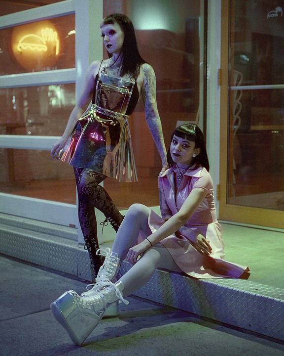 Two women pose at night in front of a building with a neon sign.