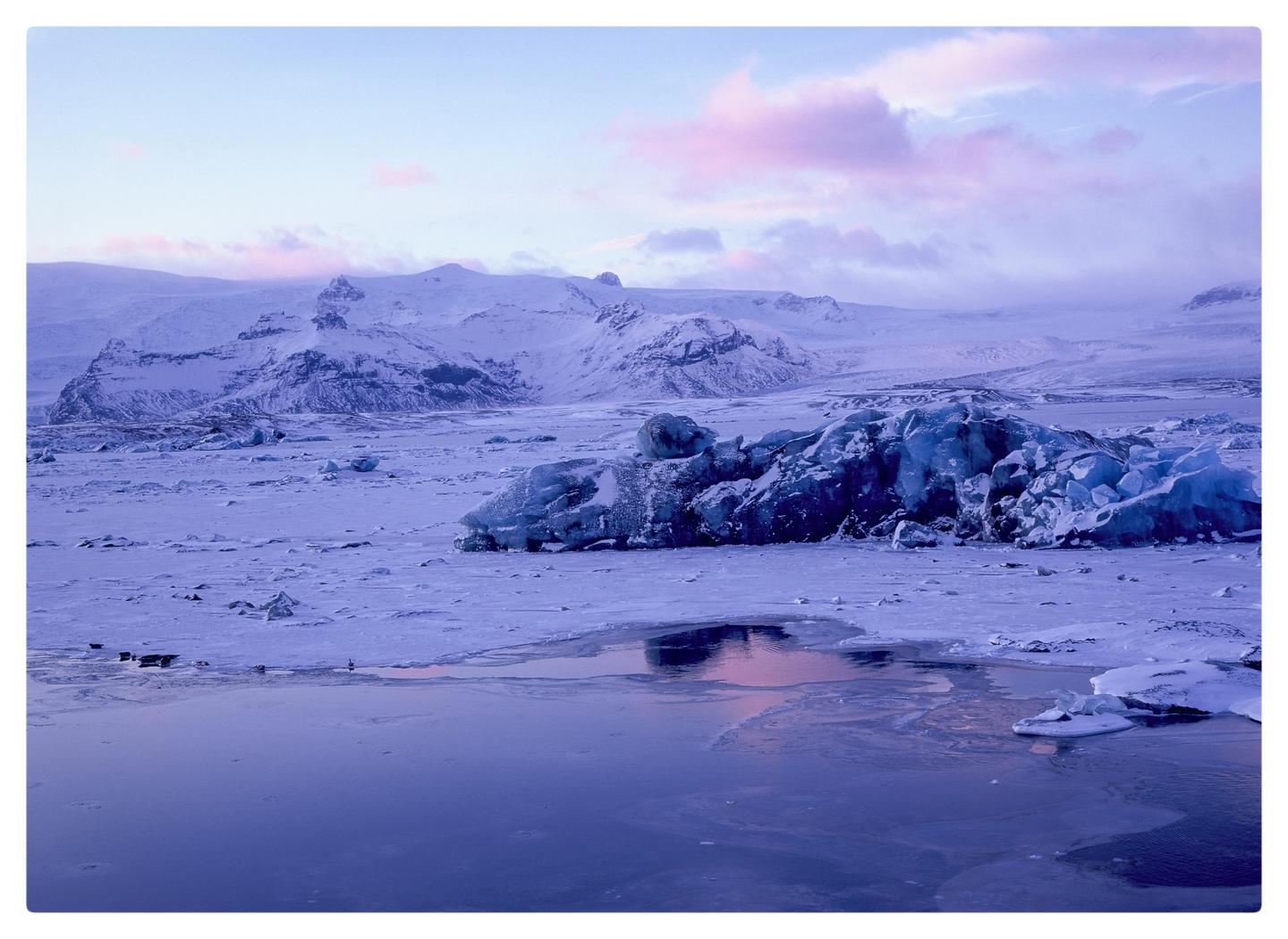 A body of water reflects the sky and mountains covered in snow and ice.
