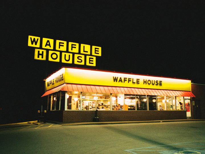 A Waffle House restaurant with bright yellow and red signs is illuminated at night.
