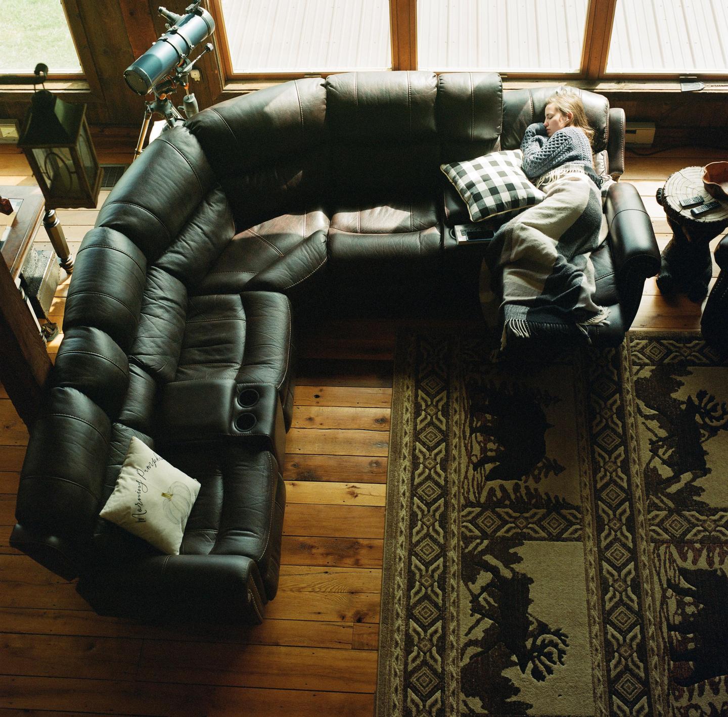 A child sleeps on a large leather sofa next to a window.