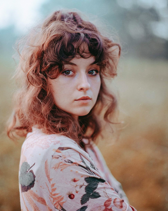 A woman with curly hair and a floral shirt looks directly at the viewer.