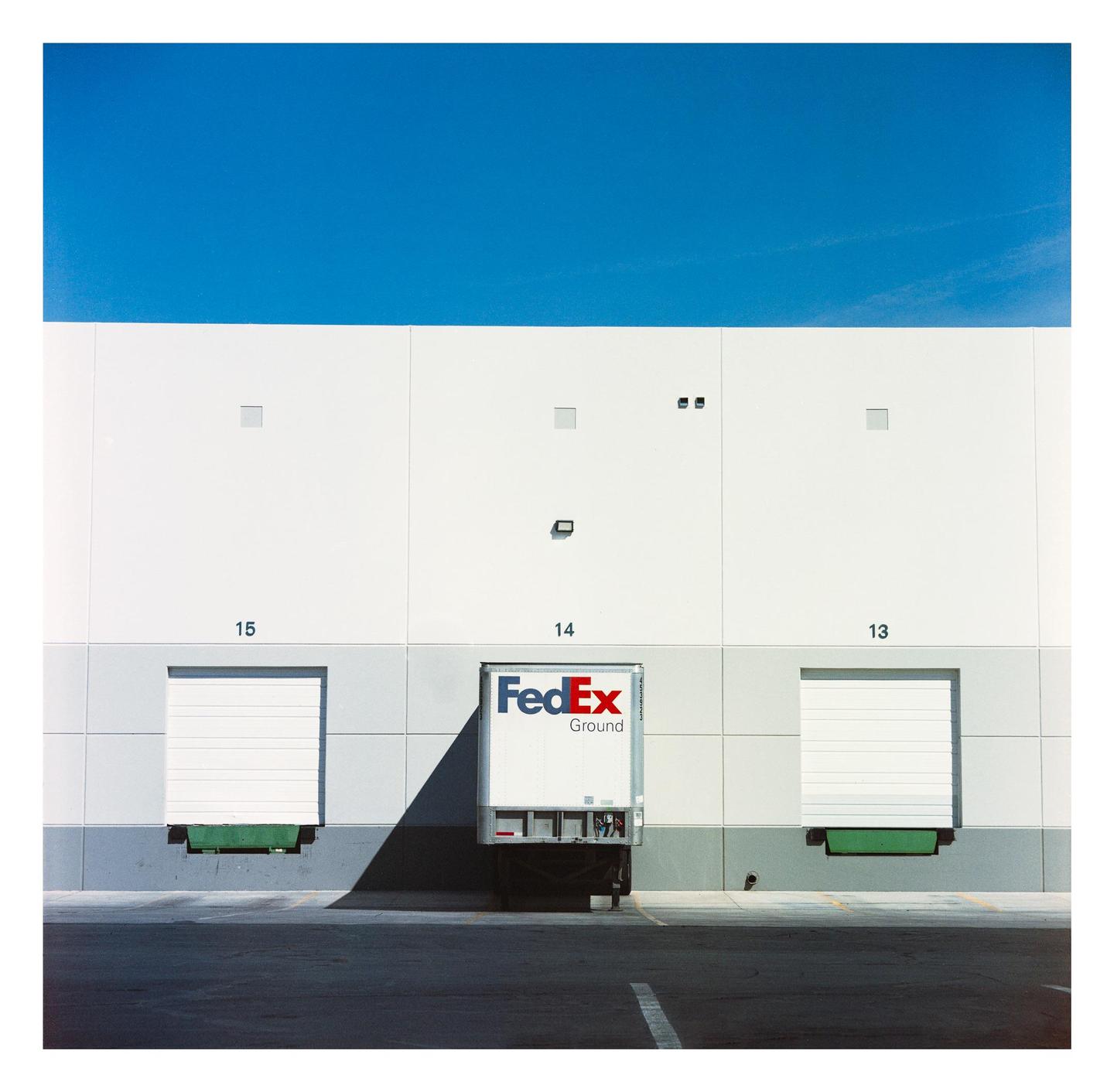 A FedEx truck is parked at a loading dock under a clear blue sky.