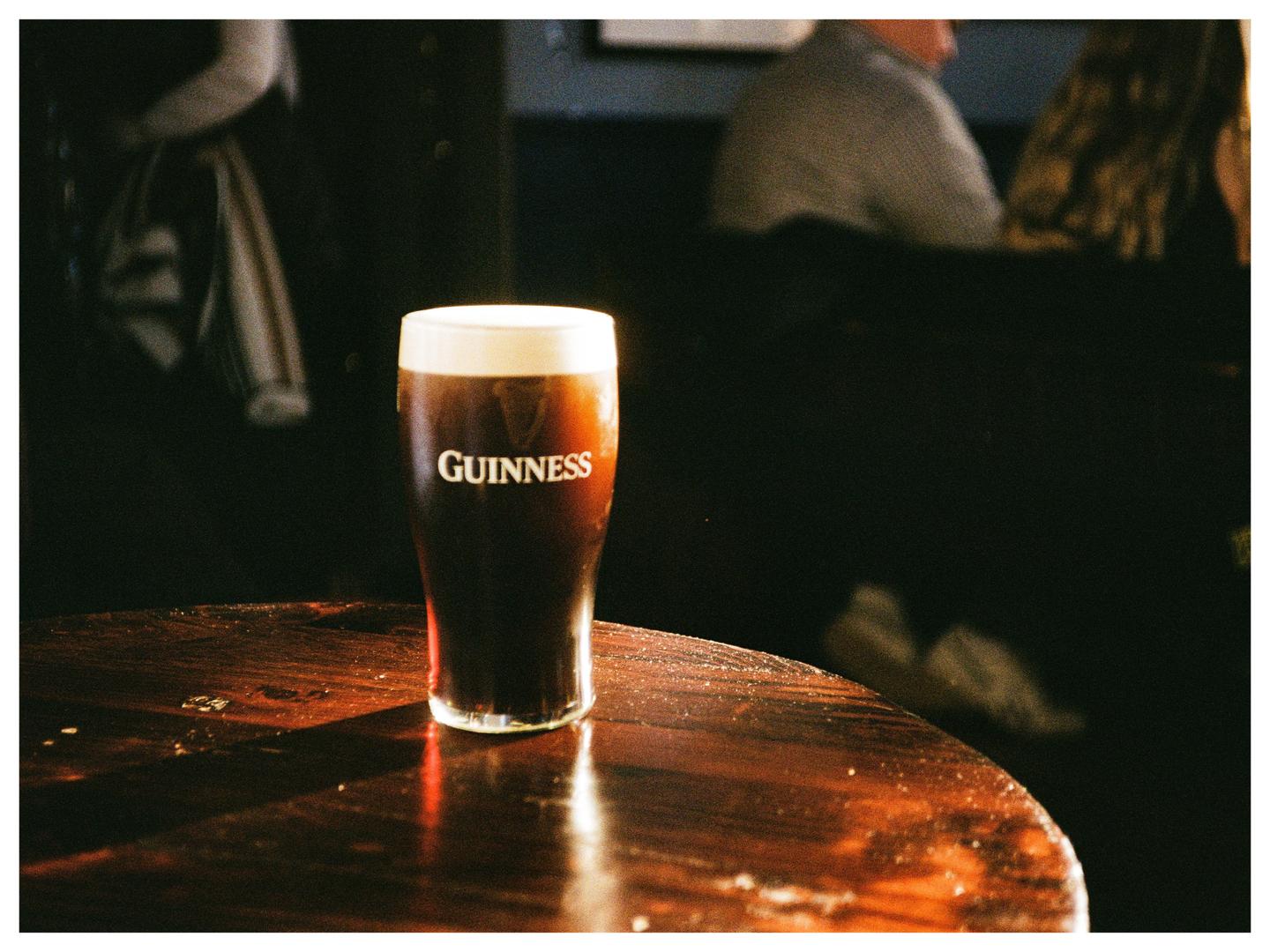 A pint of Guinness sits on a wooden table in a dimly lit pub.