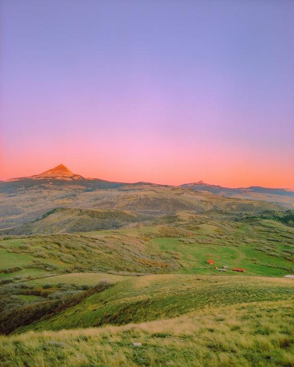 A mountain landscape with rolling green hills and a vibrant pink and purple sky at sunset.
