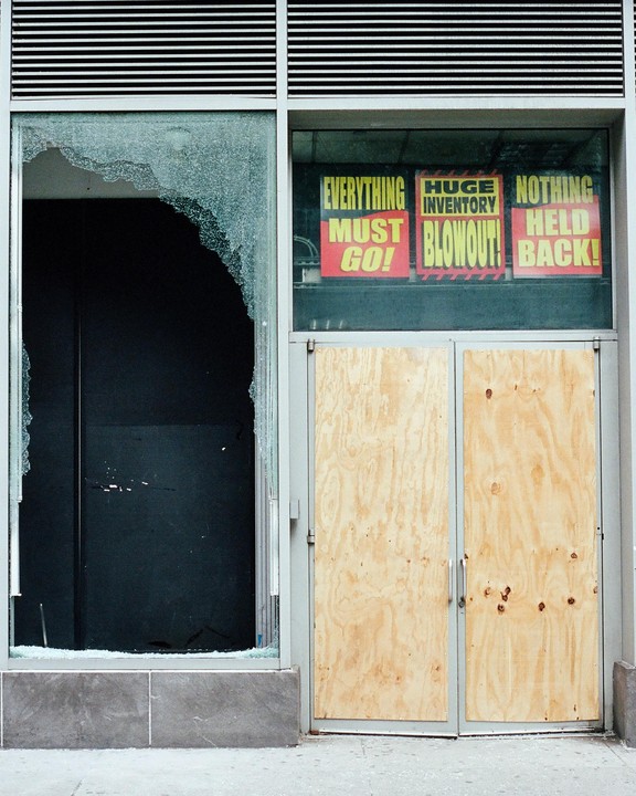 A storefront with a broken window and boarded-up doors displays "Everything Must Go" signs.
