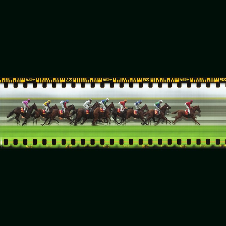 A slit-scan image shows several horses and jockeys racing on a green track.