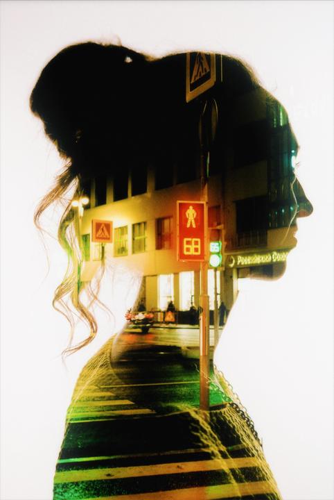 A double exposure shows the silhouette of a woman overlaid with a night street scene featuring a crosswalk, traffic lights, and buildings.