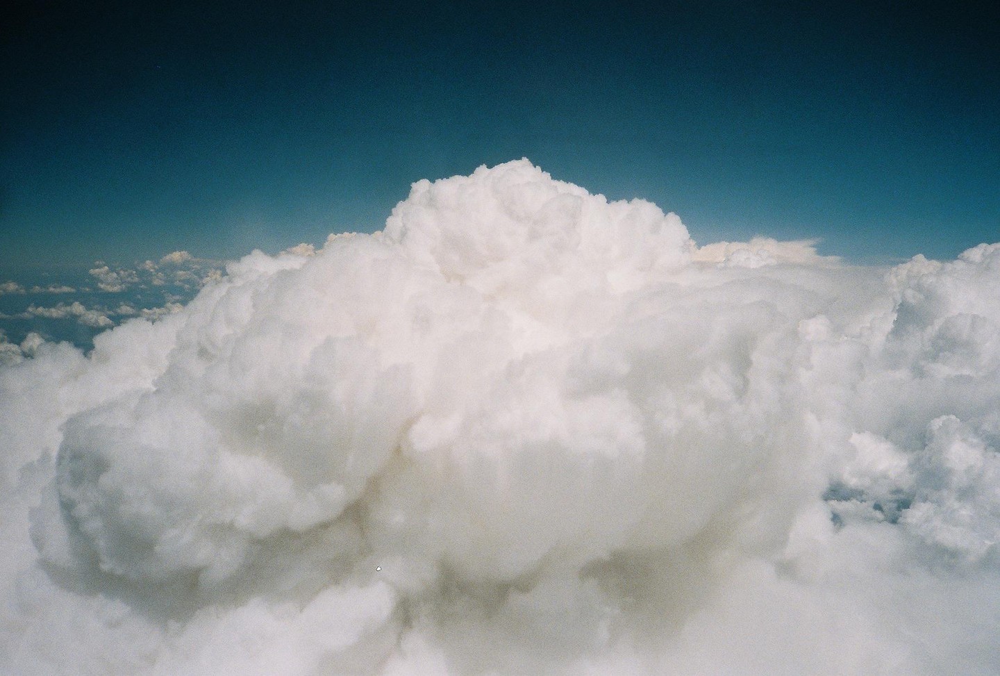 A large white cloud formation rises above other clouds under a clear blue sky.