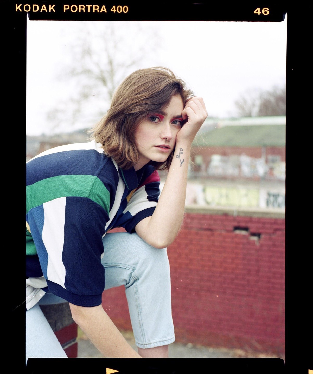 A woman with red eyeshadow and a striped shirt poses with her arm resting on her knee.