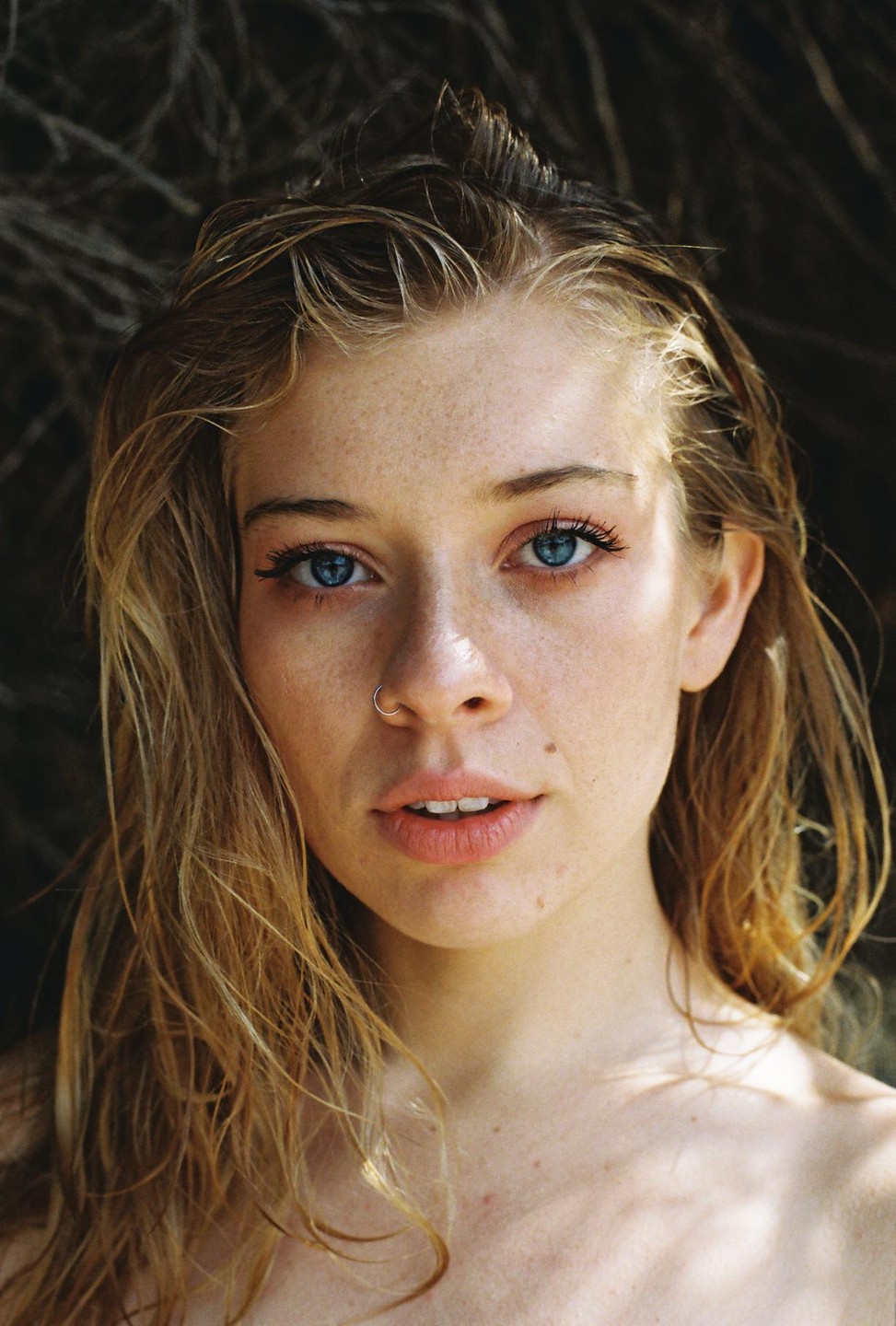 A woman with wet hair and a nose ring looks directly at the viewer.