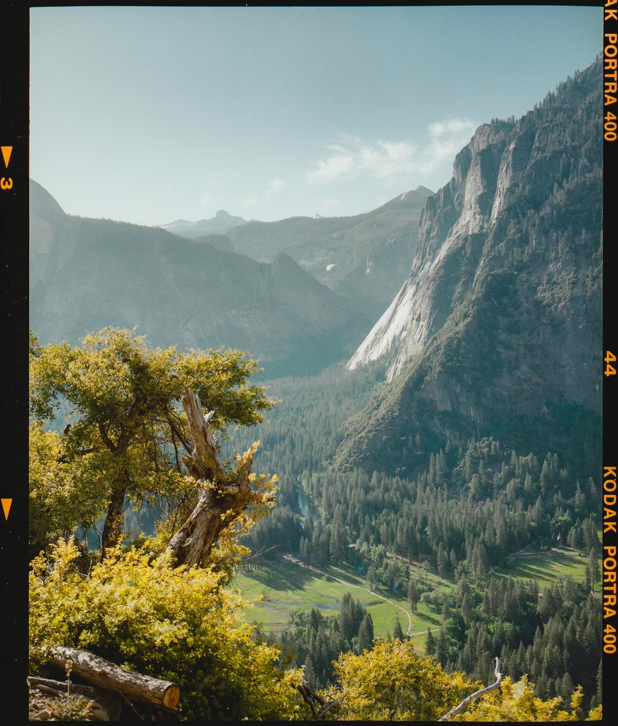 A valley with a river and forest is surrounded by mountains under a clear sky.