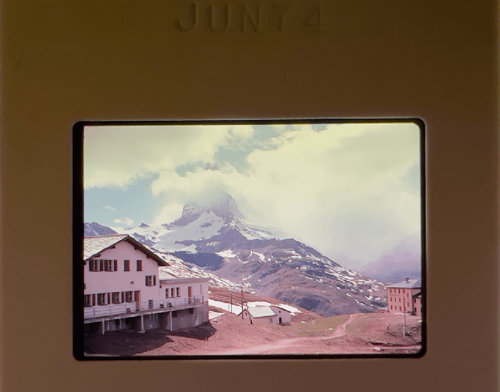 A large snow-capped mountain rises behind a village with several buildings.