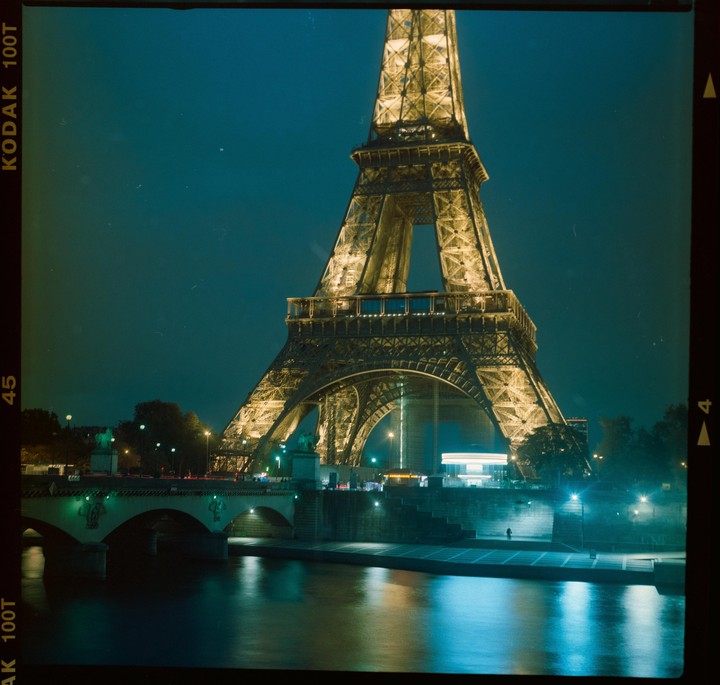 The Eiffel Tower is illuminated at night next to a bridge over a river.