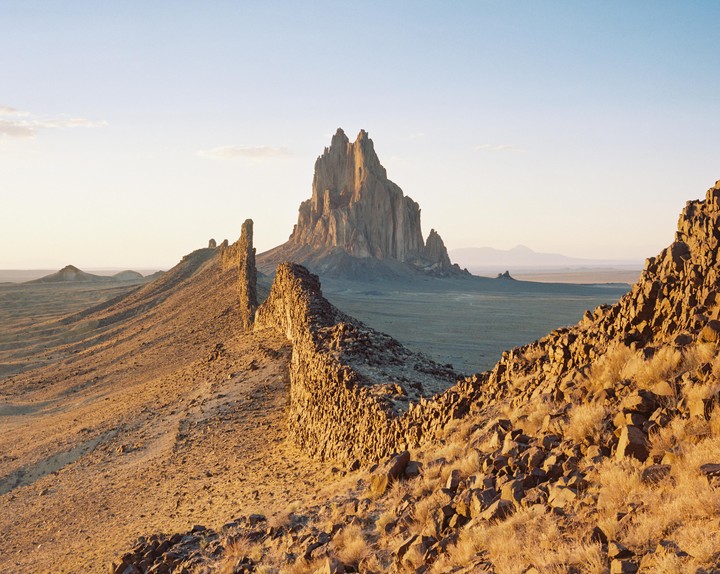 A vast desert landscape features a prominent rock formation in the distance and a long, jagged ridge in the foreground.
