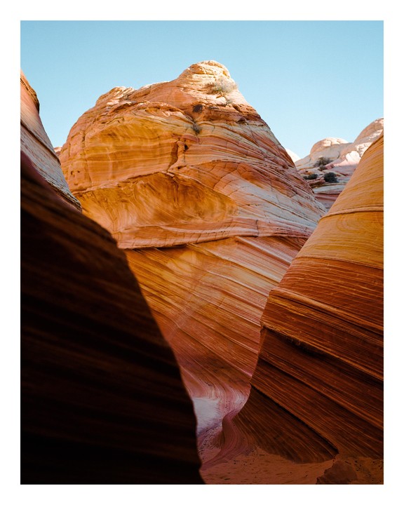 A narrow canyon with striped rock formations is illuminated by sunlight.