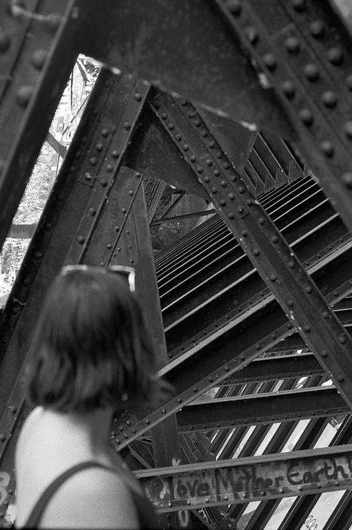 A woman stands with her back to the camera, looking at the metal structure of a bridge.