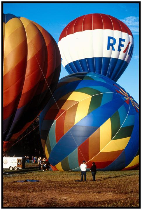 Three hot air balloons are on the ground with people standing nearby.