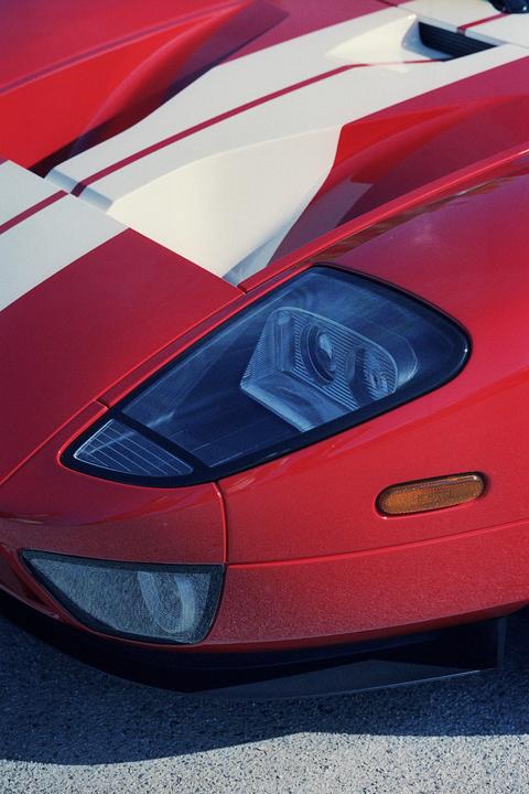 A red sports car with white racing stripes is parked on asphalt.