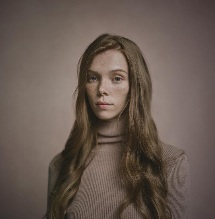 A woman with long, wavy hair and freckles looks directly at the viewer.