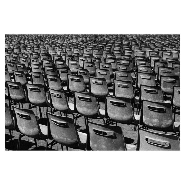 Hundreds of empty chairs are arranged in neat rows on a paved surface.
