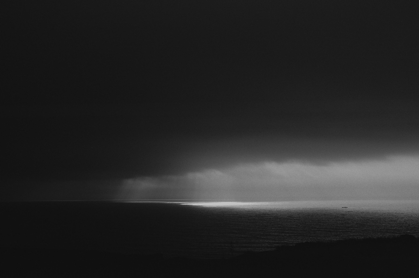 A dark ocean is illuminated by a single beam of light from the sky, with a small boat visible in the distance.
