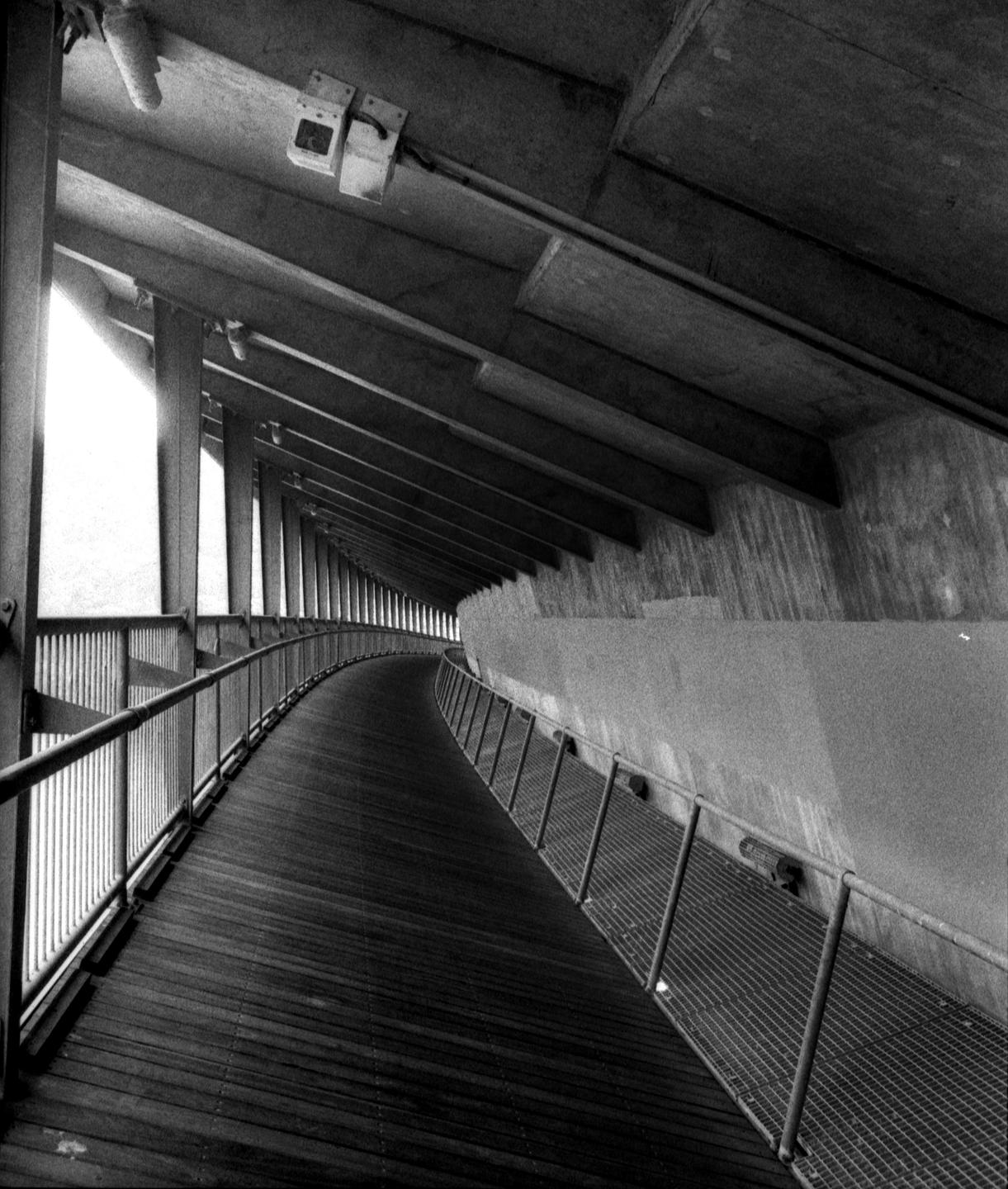 A long, curving wooden walkway with metal railings is visible under a concrete ceiling.