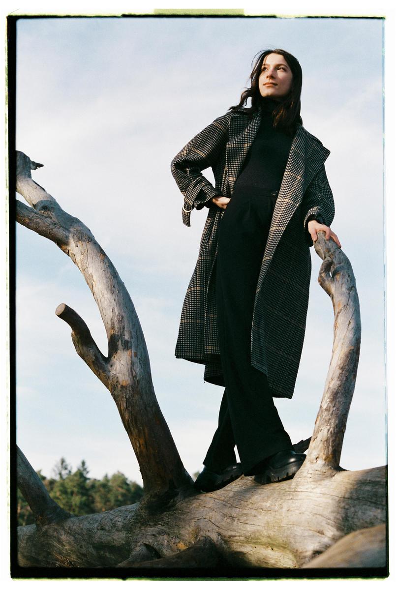 A woman stands on a large fallen tree trunk, looking up at the sky.