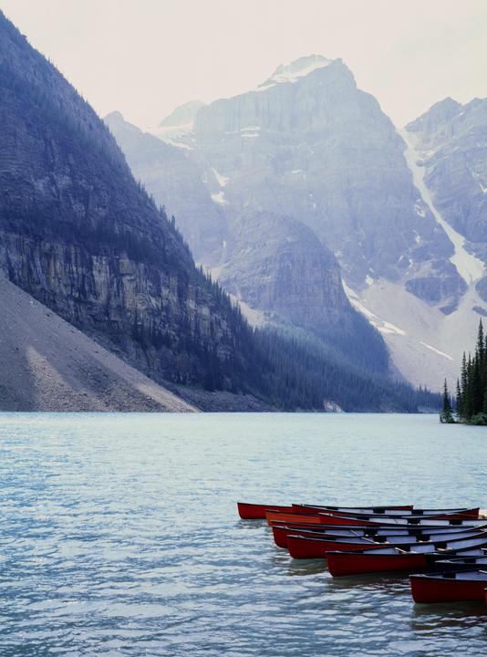 Red canoes float on a lake surrounded by mountains and pine trees.