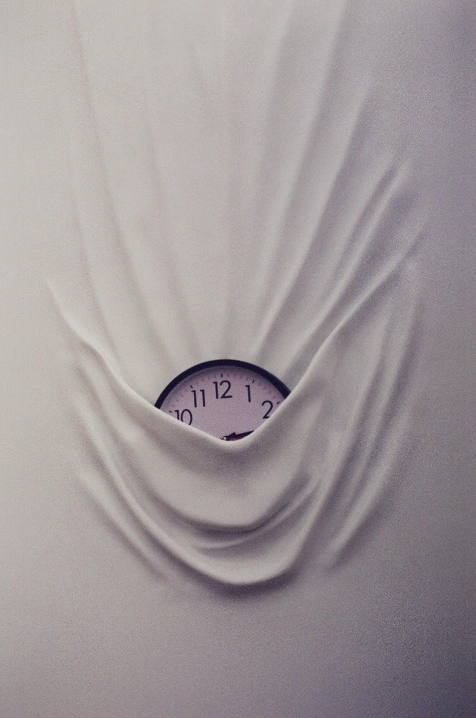 A clock face is partially visible, emerging from behind a draped white fabric.