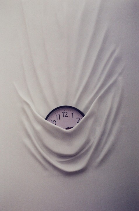 A clock face is partially visible, emerging from behind a draped white fabric.