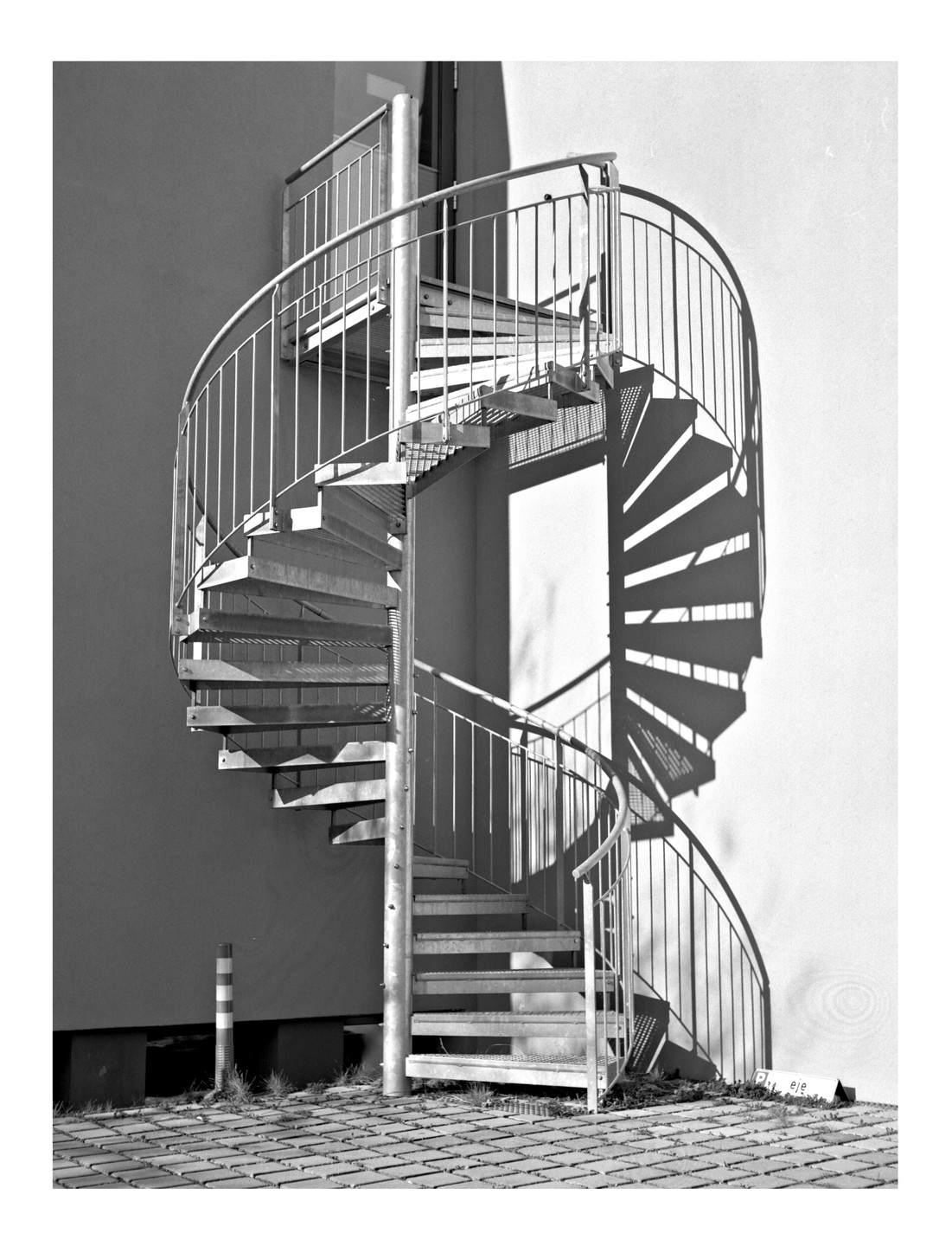 A spiral staircase casts a shadow on a building wall.