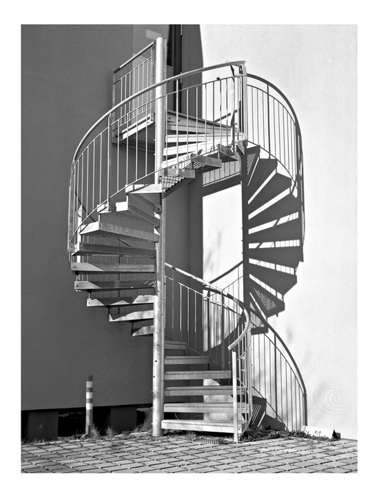 A spiral staircase casts a shadow on a building wall.