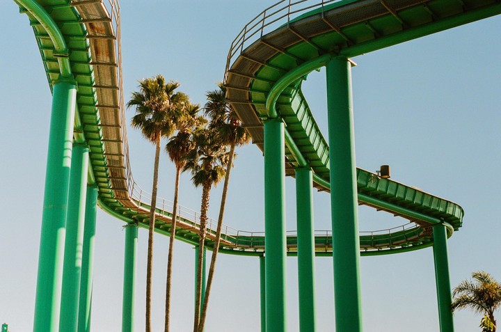 A green roller coaster track curves through the sky, with palm trees visible beneath it.