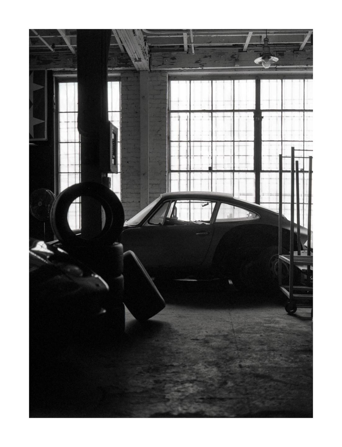 A classic car is parked in a warehouse with large windows.