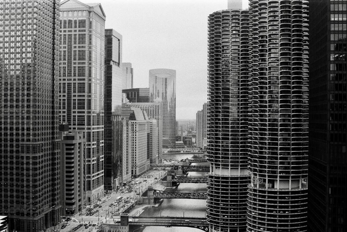 A high-angle view of the Chicago River with multiple bridges, surrounded by tall buildings and city traffic.