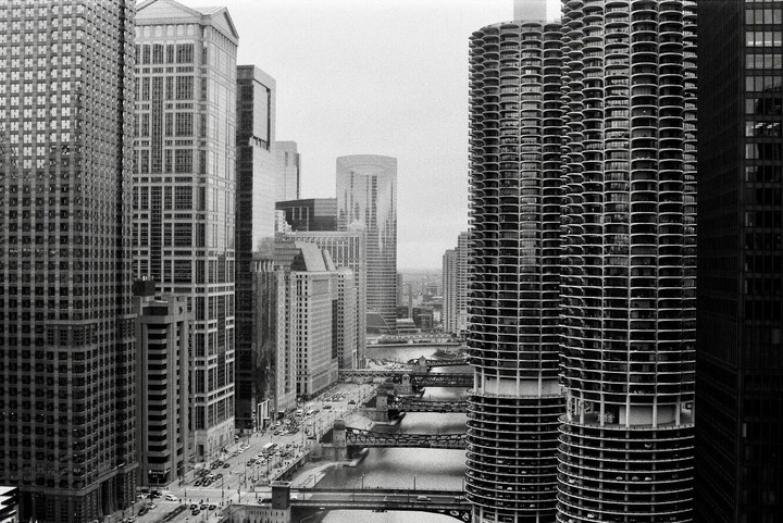 A high-angle view of the Chicago River with multiple bridges, surrounded by tall buildings and city traffic.