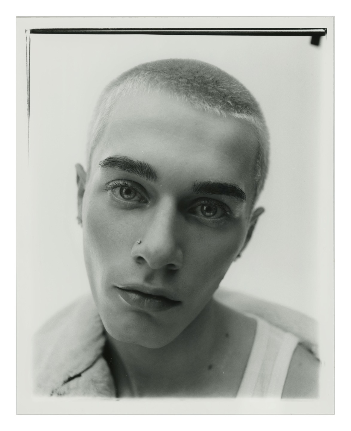 A man with a nose piercing and short hair looks directly at the viewer.