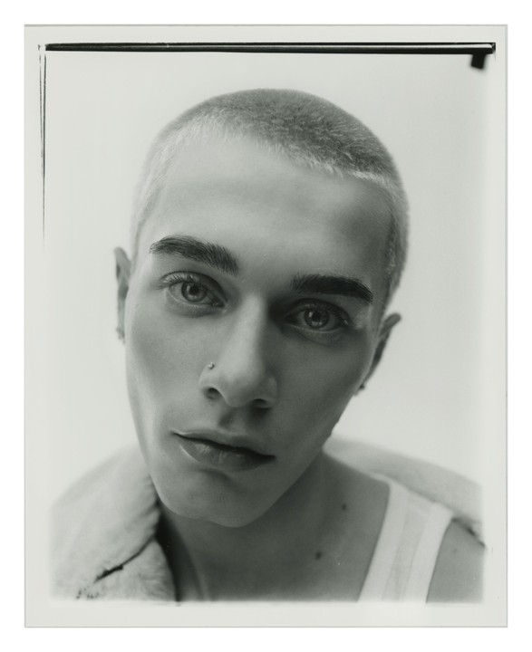 A man with a nose piercing and short hair looks directly at the viewer.